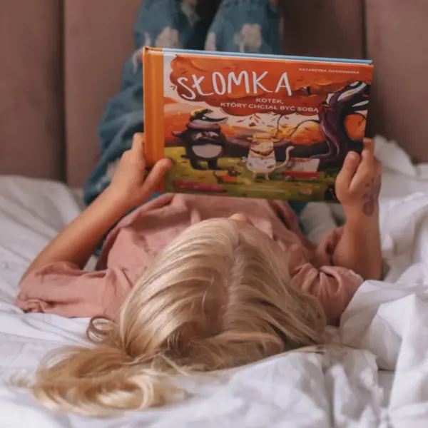 Dziewczynka czyta książkę "Słomka kotek,który chciał być sobą" Katarzyny Ogonowskiej.
